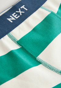 Shorts en satin rayés vert et blanc avec une ceinture élastique bleu marine portant le texte "NEXT". Tissu lisse avec des coutures contrastées.