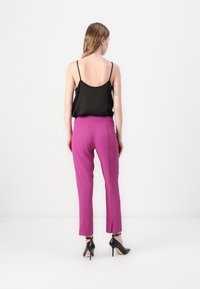 Haut noir à bretelles porté avec un pantalon rose sur mesure présentant des fentes sur les côtés ; des chaussures à talons aiguilles noires complètent la tenue.