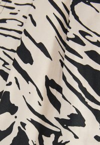 Zwart-wit zebraprintstof met een gestructureerd oppervlak, gekenmerkt door gedurfde golvende lijnen op een lichtbeige achtergrond.