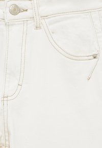 Tissu en denim blanc avec un gros plan sur une poche, présentant des coutures contrastantes beige et une fermeture à boutons métalliques.