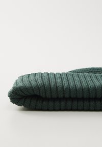 Green knitted fabric, folded with a ribbed texture and even stripes. Material appears soft and is shown against a white background.