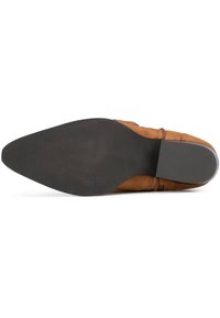 Zapato de ante marrón con punta redondeada, con suela de goma negra y un acabado liso. Incluye costuras decorativas y acentos.