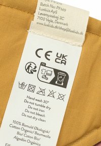 Label sewn onto a mustard-colored fabric. Contains care instructions, fabric details, and recycling symbols printed in black.