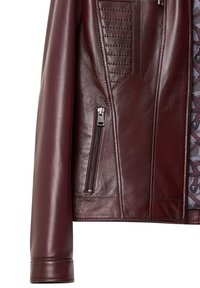 Giacca in pelle borgogna con texture trapuntata sulle spalle, tasca con zip e finitura liscia, dotata di una fodera interna decorata.