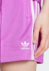 Roze atletske kratke hlače od lagane tkanine s tri bijele pruge uz stranu i adidas logotipom u bijeloj boji na donjem rubu.