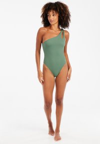 Maillot de bain une pièce vert, design asymétrique épaule unique avec un nœud accentué, texture lisse, jambes hautes découpées et construction sans coutures.