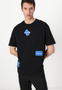 Svart bomull t-skjorte med blå merkeputer, rund hals, korte ermer og en avslappet passform. Glatt tekstur med grafiske design.
