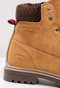 Botte de travail Tan KangaROOS avec col matelassé brun rembourré, languette de traction rouge, logo kangourou embossé et semelle en caoutchouc épaisse à rainures.