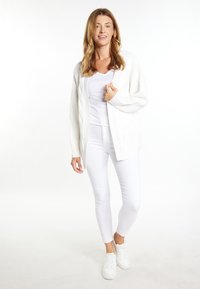 Un cardigan alb tricotat cu modele în cablu, asortat cu un top alb fără mâneci și pantaloni alb cu croi slim. Încălțămintea consta în adidași albi.