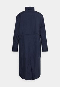 Lange, donkerblauwe jas gemaakt van een gestructureerd, lichtgewicht materiaal. Heeft een staande kraag en een rugsplits voor extra bewegingsvrijheid.