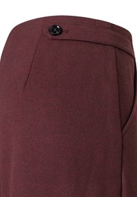 Bordeauxfarbene, maßgeschneiderte Hosen mit glatter Textur, ausgestattet mit einem einzigen schwarzen Knopfverschluss und Seitentaschen. Subtil sichtbares Fischgrätmuster.