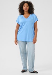 Light blue, short-sleeved V-neck t-shirt made of soft fabric, paired with light blue straight-leg jeans and black flat shoes.