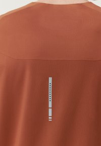 Tričko s krátkym rukávom v červeno-hnedej farbe s textúrovanou látkou. Má elegantný vertikálny grafický dizajn v svetlomodrej farbe s čiernymi akcentmi na zadnej strane.