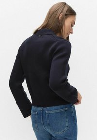 Marineblauwe gebreide trui met een kraag en lange mouwen, voorzien van een getailleerde taille en een subtiel gestructureerd patroon.