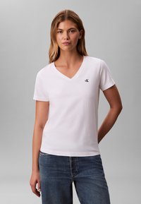 T-shirt bianca in cotone con scollo a V e maniche corte, caratterizzata da un piccolo logo nero "ck" sul petto a sinistra e orlo dritto.