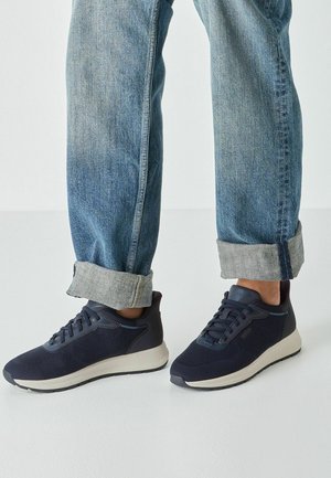 Marineblauwe gaas sneakers met een gladde neuskap en lichtgekleurde zool, gecombineerd met opgerolde blauwe spijkerbroek.