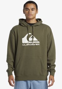 Olive green hoodie with a front pocket, featuring a large white Quiksilver logo. Material appears soft with a relaxed fit and adjustable drawstring hood.
