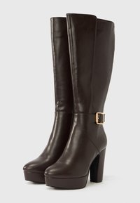 Σκούρα καφέ δερμάτινες μπότες μέχρι το γόνατο με πλατφόρμα και τακούνι, με χρυσή αγκράφα στη εξωτερική πλευρά κάθε μπότας.