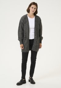 Cardigan gri tricotat, cu croială oversized și deschidere în față, prevăzut cu manșete și tiv cu dungi. Asortat cu pantaloni negri skinny și pantofi negri.