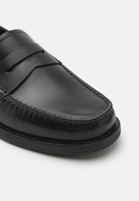Schwarze Lederloafer mit einer glatten Oberfläche, ausgestattet mit genähten Akzenten und einer runden Zehenpartie. Die Sohle ist flach und strukturiert für besseren Halt.