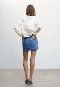 Witte gebreide trui met een losse pasvorm en textuur, gecombineerd met een blauwe denim minirok. Heeft een hoge taille en achterzakken, gedragen met grijze hakken.