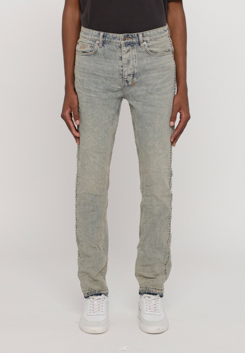 Jasnoniebieskie dżinsy o slim fit, z wyblakłą teksturą, pięcioma kieszeniami i subtelnymi detalami stębnowania. Noszone z białymi trampkami.