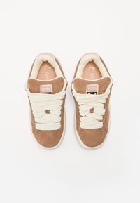 Brown suede sneakers with white laces, round toe, padded collar, and branded tags on the tongue. Light pink accents at the heel.