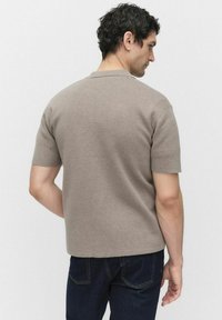 Korte mouwen, beige gebreide trui met een gestructureerde afwerking en een ronde halslijn, gecombineerd met donkerblauwe spijkerbroek. Zicht van achteren.