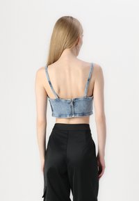 Denim kratka majica s tankim naramenicama, svijetlo plave boje, zatvaranje na zip sprijeda i prilagođenog dizajna. Uparena s crnim hlačama visokog struka.