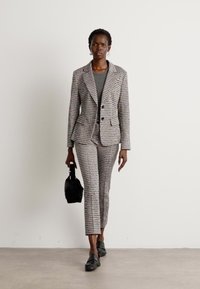 Tweed blazer and matching trousers in muted gray, pink, and white tones. Worn with a gray top and black handbag. Black loafers complete the outfit.