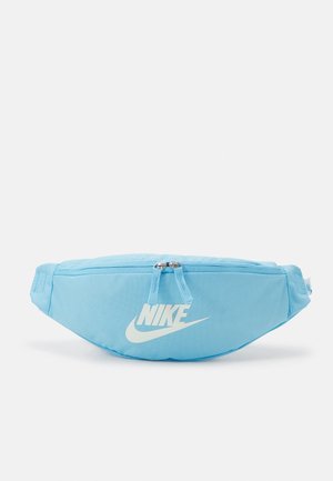 Banane Nike bleu clair avec logo blanc, double fermeture éclair et sangle ajustable sur fond blanc.