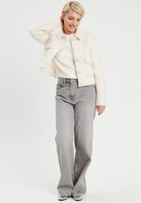 Veste cropped en mélange de laine blanche avec des boutons, poche poitrine et coupe décontractée, assortie à un jean large gris et des talons métalliques.