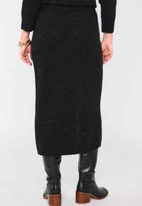 Jupe midi en tricot noir avec une surface texturée ornée de paillettes dorées. L'ourlet présente des détails à côtes, associée à des bottes noires montantes.