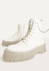 Vita ankelstövlar med en kraftig, genomskinlig sula. Tillverkade i mjukt läder med snörning framtill och dragkedja på sidan. Har sydda detaljer.