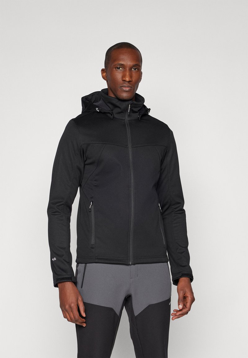 Giacca nera con chiusura a zip, cappuccio regolabile e due tasche laterali. Presenta una texture liscia e un design aderente, abbinata a pantaloni grigi.