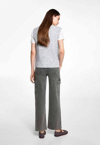 Grå kabelstickad väst över en vit T-shirt, i kombination med vida grå cargobyxor. Texturerade material med fickor på byxorna och slip-on skor.