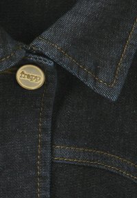 Dunkles Jeanshemd mit spitzem Kragen, goldfarbenen Nähten und einem Metallknopf mit dem Markennamen "frapp" gut sichtbar darauf.