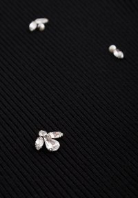 Trois petits groupes de strass transparents et de perles disposés sur une surface en tissu noir côtelé.