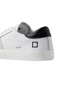 Sneaker bianco in pelle con dettagli in suede grigio e tallone nero. Presenta un design minimalista con un logo quadrato e suola piatta bianca.