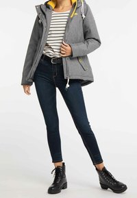 Grå huva jacka med gul foder, randig topp, mörkblå tajta jeans och svarta snörstövlar. Har dragkedjor och dragsko.