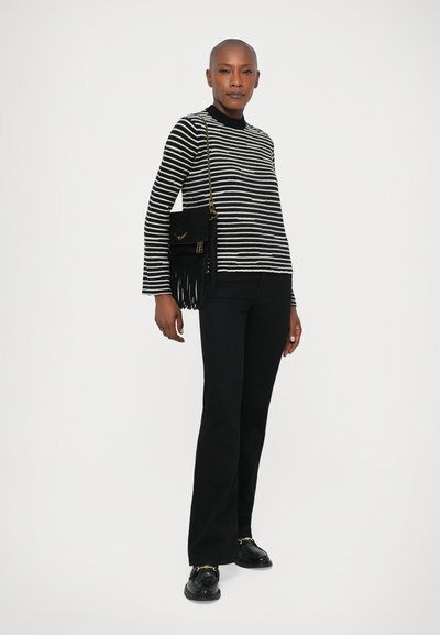 Maglione a righe bianche e nere in maglia con collo alto, abbinato a pantaloni neri a zampa d'elefante e una borsa nera con frange. Mocassini neri completano il look.