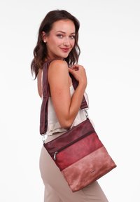 Červená a růžová kožená kabelka přes rameno se zipovou přední kapsou, nastavitelného popruhu a hladkým, strukturovaným povrchem. Obsahuje akcent s logem.