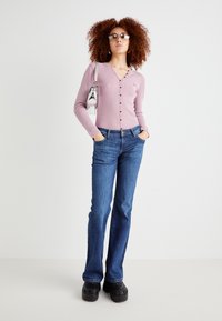 Maglietta a maniche lunghe a coste rosa chiaro con dettagli a bottoni e scollatura rotonda, abbinata a jeans a zampa blu e zoccoli neri con plateau.