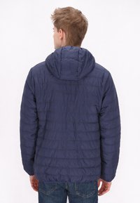 Marineblauwe gewatteerde jas met capuchon, met een horizontaal gestikt ontwerp en een gladde textuur, aangevuld met casual jeans.