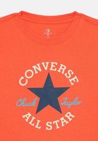 Oranje katoenen T-shirt met een grote marineblauwe sterafbeelding en de teksten "CONVERSE ALL STAR" en "Chuck Taylor" in blauw en wit.