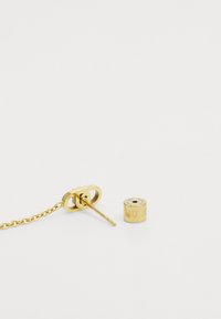 Boucles d'oreilles dorées avec un maillon de chaîne et un clou cylindrique, ornées d'un logo gravé. Surface lisse avec un design moderne et épuré.