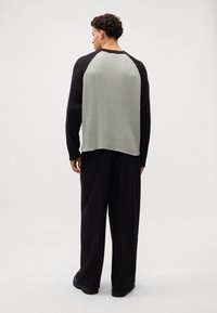 Strickpullover mit schwarzen gerippten Ärmeln und hellgrauer gerippter Rückseite. Lockere Passform, lange Ärmel und runder Halsausschnitt. Kombiniert mit schwarzen weit geschnittenen Hosen.