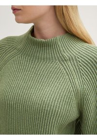 Groene geribbelde gebreide trui met hoge hals, voorzien van textuurlijnen in verticale richting en een aansluitend ontwerp dat zich naar het lichaam vormt.