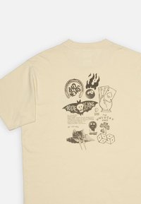 T-shirt a maniche corte color crema chiaro con design grafici neri, tra cui teschi, carte da gioco ed elementi testuali sul retro.