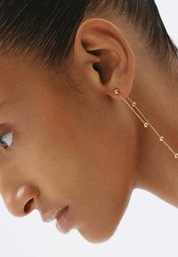 Pendientes de cadena dorada con pequeños acentos esféricos. Las cadenas cuelgan por debajo del lóbulo de la oreja, exhibiendo un diseño elegante y una textura brillante.